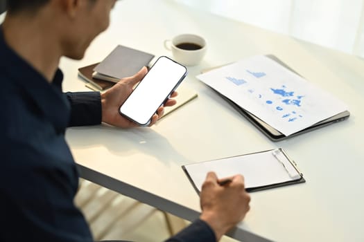 Male employee sitting at working desk and using smartphone. Blank screen for graphic display montage.