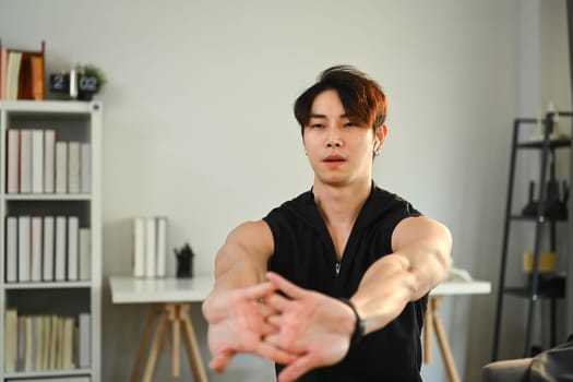 Athletic man in sportswear stretching arms before workout routine at home. Fitness, training and healthy lifestyle concept.