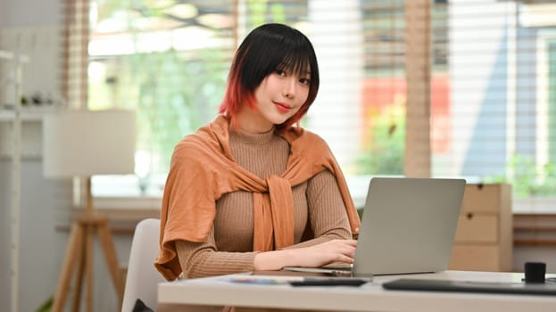 Beautiful young stylish woman using laptop at modern home office. Freelance, creative occupation, e-learning concept.