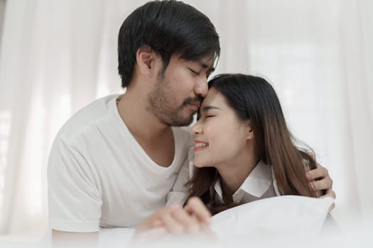 Asian Romantic couple in bed enjoying sensual foreplay Happy sensual young couple lying in bed together. Beautiful loving couple kissing in bed