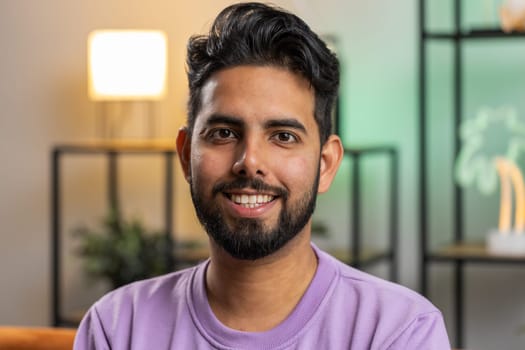 Portrait of happy calm indian man at home couch smiling friendly, glad expression looking away dreaming resting, relaxation feel satisfied concept good news, celebrate win. Hindu guy in living room