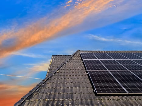 Colorful sunset on solar panels producing clean energy on a roof of a residential house