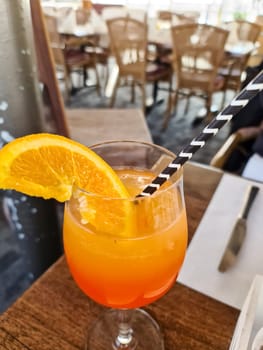 An orange cocktail with a straw and an orange slice in a glass with a soft background of a restaurant