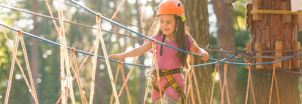 Adorable little girl enjoying her time in climbing adventure park on warm and sunny summer day. Summer activities for young kids. Child having fun on school vacations.