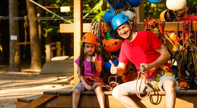Adorable little girl enjoying her time in a rope playground structure at adventure park, her father supporting her, family weekend activities