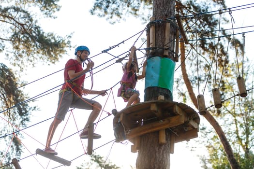 Adorable little girl enjoying her time in a rope playground structure at adventure park, her father supporting her, family weekend activities