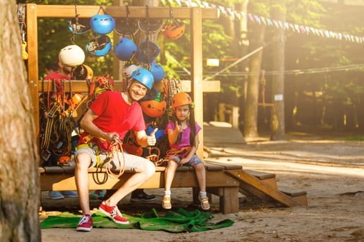 Young father helps his daughter on the obstacle in the rope park.