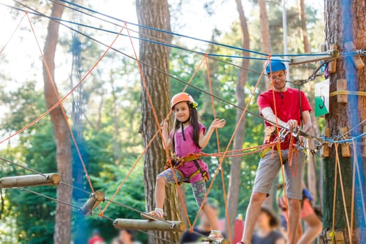 Young father helping his little daughter in the rope park