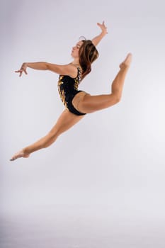 Flexible girl, rhythmic gymnastic artist jumping on white dark background. Grace in motion, action.