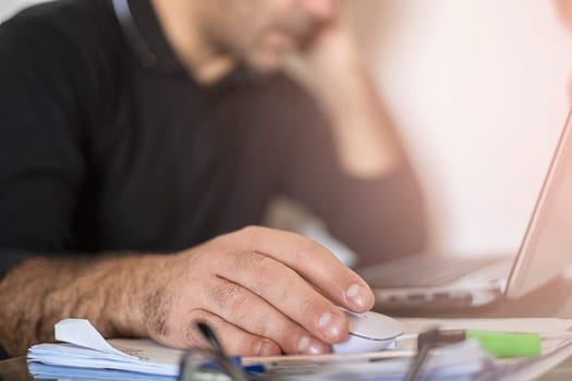 A man's using laptop hand on mouse and thinks.