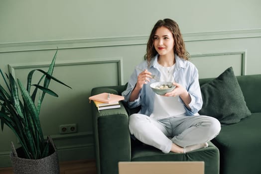 Contented Student Taking a Break from Online Classes: Food, Books, and Laptop on Sofa. Happy Female Student Taking a Break from Online Studies with Delicious Meal and Books.