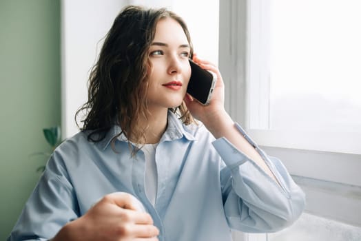 Caring wife by the window eagerly awaiting her husband's arrival. Anxious wife calling her husband while keeping an eye on the clock. Loving wife anxiously awaiting her husband's return from work