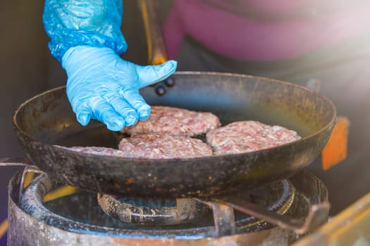 The hands of the cook prepare cutlets from minced pork in a frying pan. Fast food restaurant on the street. High quality photo