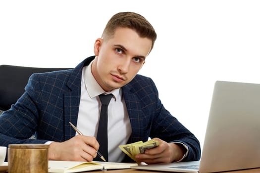 young businessman working on laptop and holding money while sitting on chair at desk.