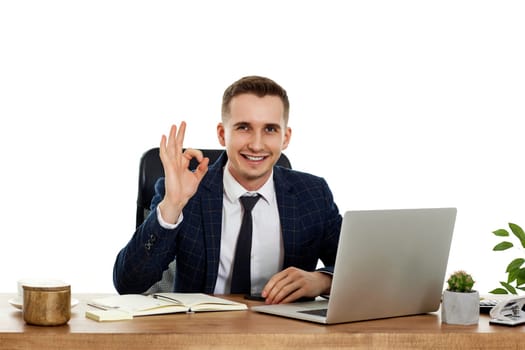 young happy businessman sitting at desk working on laptop pc computer and showing Ok gesture