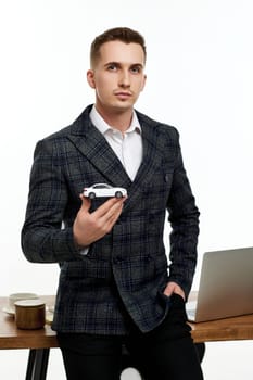Successful caucasian businessman holding a toy car while standing at desk. Car dealerships offer car . Car insurance