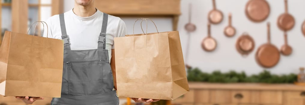 Courier holding paper bags with food, space for text. Delivery service.