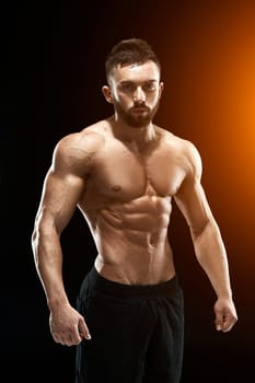 Muscular bodybuilder guy doing posing over black background. with sun flare