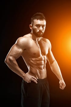 Muscular bodybuilder guy doing posing over black background. with sun flare