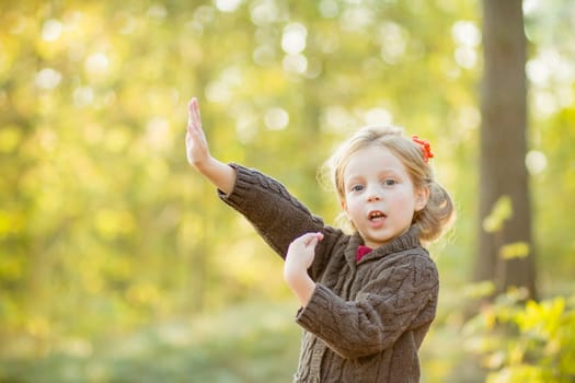 Young happy and smiling mom with her little daughter in arms hugging and kissing spending a weekend on a walk in autumn park.