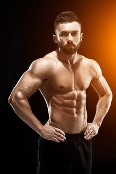 Muscular bodybuilder guy doing posing over black background. with sun flare