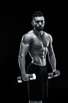 Muscular bodybuilder guy doing posing over black background. dumbbells in his hands. doing exercises Black and white color