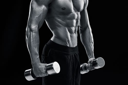 Muscular bodybuilder guy doing posing over black background. dumbbells in his hands. doing exercises. close up. Black and white color
