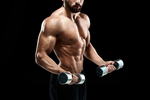 Muscular bodybuilder guy doing posing over black background. dumbbells in his hands. doing exercises. close up