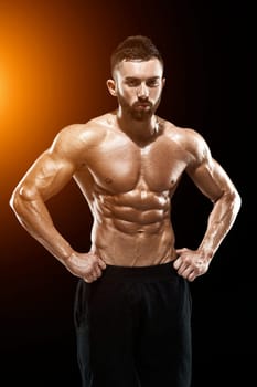 Muscular bodybuilder guy doing posing over black background.. with sun flare