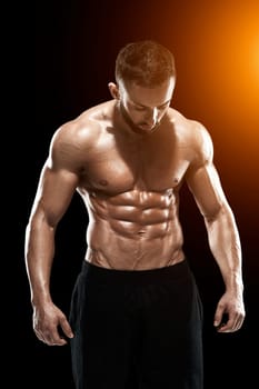 Muscular bodybuilder guy doing posing over black background.. with sun flare