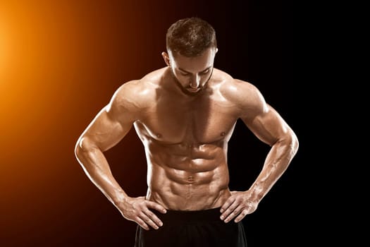Muscular bodybuilder guy doing posing over black background.. with sun flare