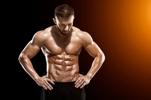 Muscular bodybuilder guy doing posing over black background.. with sun flare