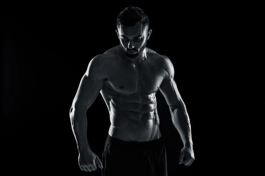 Muscular bodybuilder guy doing posing over black background. Black and white color