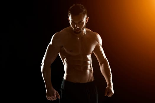Muscular bodybuilder guy doing posing over black background.. with sun flare
