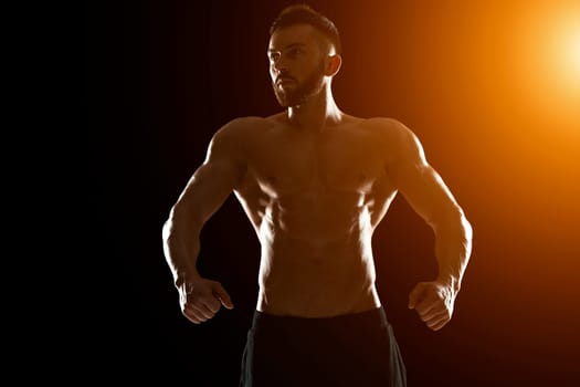 Muscular bodybuilder guy doing posing over black background.. with sun flare