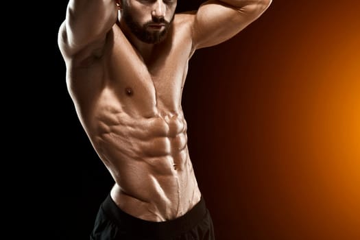 Muscular bodybuilder guy doing posing over black background. Close up. with sun flare