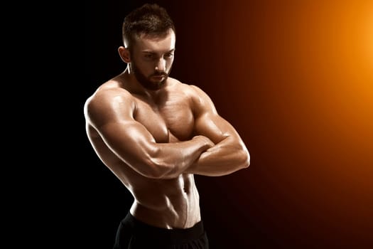 Muscular bodybuilder guy doing posing over black background.. with sun flare
