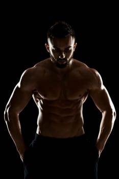 Image of very muscular man posing with naked torso in studio on black background.