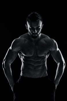 Image of very muscular man posing with naked torso in studio on black background. Black and white color