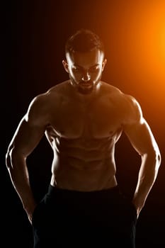 Image of very muscular man posing with naked torso in studio on black background.. with sun flare