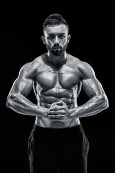 Image of very muscular man posing with naked torso in studio on black background. Black and white color