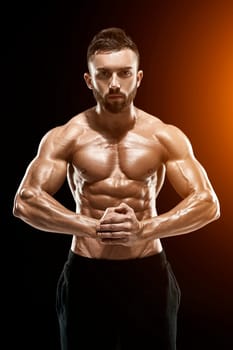 Image of very muscular man posing with naked torso in studio on black background.. with sun flare