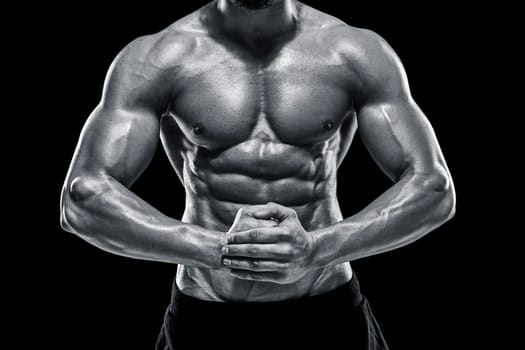 Image of very muscular man posing with naked torso in studio on black background. Black and white color