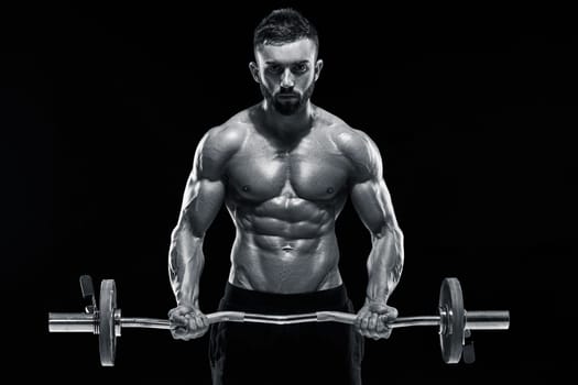 Close up of young muscular man lifting weights over dark background. Black and white color