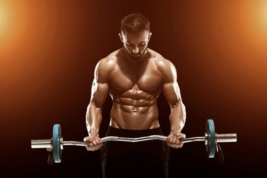 Close up of young muscular man lifting weights over dark background. with sun flare