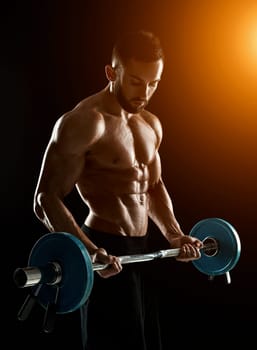 Close up of young muscular man lifting weights over dark background. with sun flare