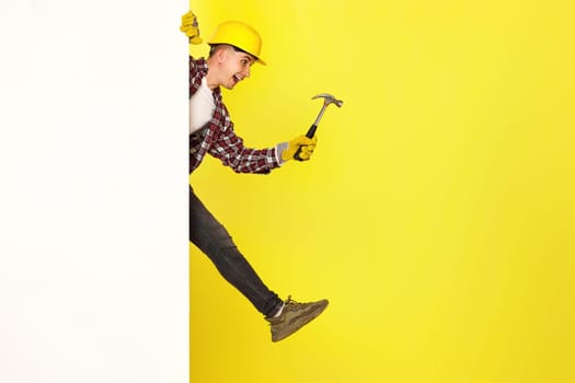 professional builder in work clothes, helmet holds hammer and comes out from behind the banner. copy space for text