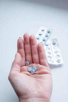 Pills, tablets and drugs heap in doctor's hand on blue background
