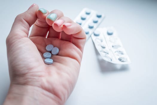 Pills, tablets and drugs heap in doctor's hand on blue background