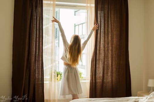 Hand Opens Curtain on the Wooden Cottage House Window. Bright Sunlight Shines Through. Beautiful snowy Winter morning light behind the Chalet Window.
